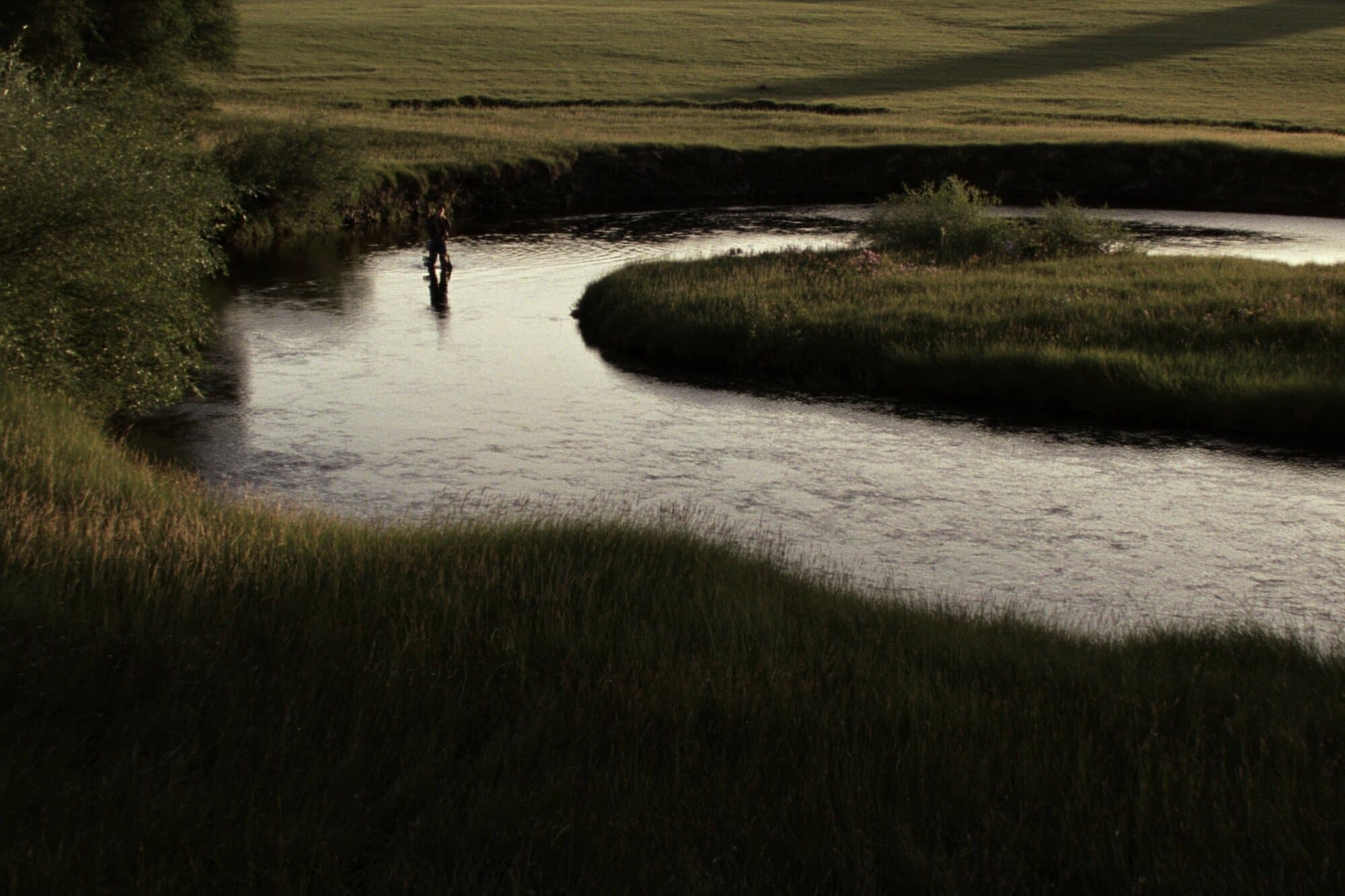 A lone angler casting on a private spring creek winding through a meadow in the late evening.
